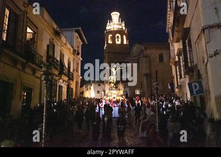 Nazarenos portant des capots en forme de cône rouge portent une plate-forme massive de la Crucifixion pendant la procession silencieuse de minuit marquant le Vendredi Saint à la semaine Sainte ou Semana Santa, 6 avril 2023 à Ronda, Espagne. Ronda, établie pour la première fois au 6th siècle avant Jésus-Christ, organise des processions de la semaine Sainte depuis plus de 500 ans. Banque D'Images