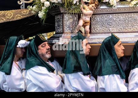 Nazarenos portant des chapeaux verts porte une plate-forme massive avec une statue de la Vierge Marie dans une procession pendant la semaine Sainte ou Santa Semana, 5 avril 2023 à Ronda, Espagne. Ronda, établie pour la première fois au 6th siècle avant Jésus-Christ, organise des processions de la semaine Sainte depuis plus de 500 ans. Banque D'Images