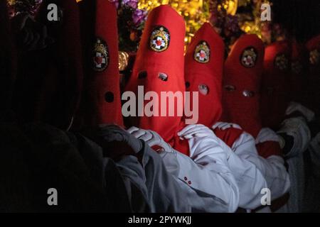 Nazarenos portant des capots en forme de cône rouge portent une plate-forme massive de la Crucifixion pendant la procession silencieuse de minuit marquant le Vendredi Saint à la semaine Sainte ou Semana Santa, 6 avril 2023 à Ronda, Espagne. Ronda, établie pour la première fois au 6th siècle avant Jésus-Christ, organise des processions de la semaine Sainte depuis plus de 500 ans. Banque D'Images