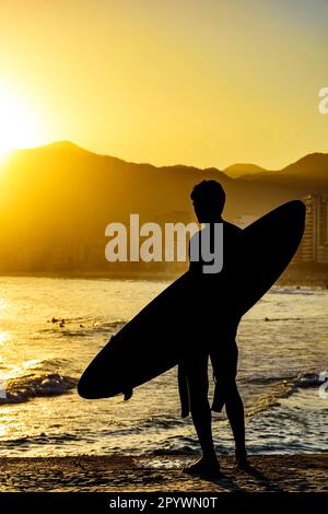 Surfeur silhouette avec sa longboard regardant les vagues de la plage d'Iapnema à Rio de Janeiro pendant le coucher du soleil, au Brésil Banque D'Images