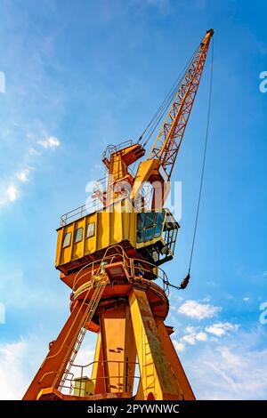 Grue jaune ancienne et obsolète sur la jetée du port vue d'en dessous et éclairée par le soleil de l'après-midi avec le ciel bleu en arrière-plan., Brésil Banque D'Images