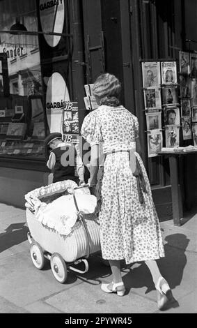 'Une femme pousse une poussette devant une exposition du kiosque de journal ''Sander' (probablement dans le centre-ville de Braunschweig). Dans l'exposition, entre autres, les magazines ''Illustrierter Beobachter'', ''Wehrfront'', ''Aquator' et ''Filmweh''.' Banque D'Images