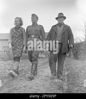 Une jeune femme, un soldat, probablement en congé à domicile, et un homme âgé traversent un champ près de Neustrelitz. En arrière-plan, une ferme. Photo non datée. Banque D'Images