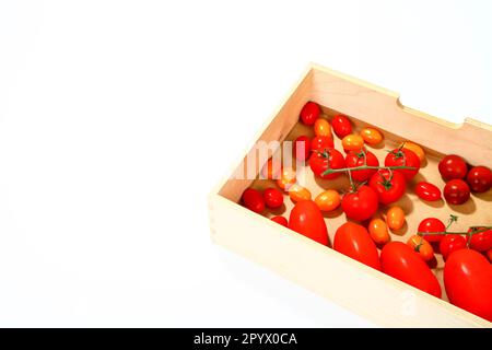 Tomates prune et cerise dans une boîte en bois isolée sur fond blanc avec espace de copie Banque D'Images