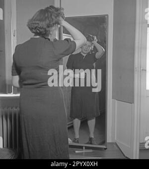 Une femme dans une robe sombre se tient devant un miroir et regarde inquiet à son corps pendant qu'elle a mis une main sur son ventre, elle pille ses cheveux avec l'autre. Banque D'Images