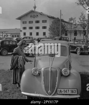 Une femme déverrouille une Fiat Topolino garée de Berlin. L'arrêt de repos sur le Reichsautobahn Munich-Salzbourg en arrière-plan a été ouvert en 1937 et est maintenant utilisé comme clinique. Banque D'Images