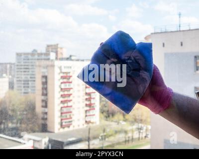 gants essuie-mains verre de fenêtre avec serviette bleue pendant le lavage de la fenêtre dans l'appartement dans la maison de ville en hauteur le jour ensoleillé de printemps Banque D'Images