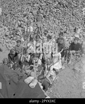 Photo non datée d'un groupe d'enfants regardant un spectacle de marionnettes parmi des piles de briques restantes des ruines. Les briques servent de rideau du théâtre de marionnettes (ci-dessous à gauche voilé par des couvertures). En arrière-plan, plus de piles de briques. Banque D'Images