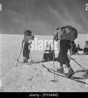 'Vue d'un groupe de skieurs montant un haut pâturage alpin dans un centre de loisirs de l'organisation nazie ''Kraft durch Freude'' (la force par la joie) dans les Alpes, tandis que d'autres prennent une pause. Le skieur avant porte un cadre arrière avec étagère, le skieur arrière un sac à dos.' Banque D'Images