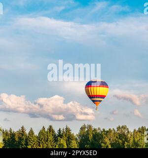 Un ballon d'air chaud lumineux vole dans le ciel bleu au-dessus des arbres de la forêt. Couleurs vives et chaudes Banque D'Images