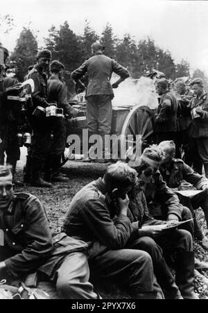 Des soldats allemands lisant un journal de front pendant une pause dans la marche. En arrière-plan, la nourriture est servie. Photo: Müller. [traduction automatique] Banque D'Images