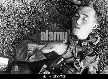 Sur le front de l'est : un soldat s'est endormi lors d'une pause dans la marche sur le front de l'est. Un cigare est allongé sur son uniforme, qui est tombé de sa main. Sa tête repose sur le masque à gaz peut. Photo: Kühn [traduction automatique] Banque D'Images
