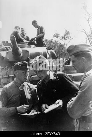 Détenteur de la Croix de Chevalier Premier lieutenant Ernst-Georg Buchterkirch (à gauche), Panzer Regiment 6, lors d'un exposé de situation avec d'autres officiers de Wehrmacht dans un village biélorusse dans la partie centrale du Front de l'est. En arrière-plan, un Panzer III [traduction automatique] Banque D'Images