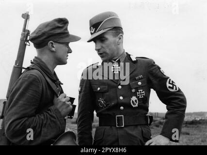 Un officier très décoré (Oberstfeldmeister / Hauptmann) du Reich Labour Service parle à un membre de la RAD affecté à la garde lors d'une visite au mur de l'Atlantique. En plus de la Croix de Chevalier, il est décoré de la Croix allemande en or, de l'insigne d'infanterie tempête et de la Croix de fer I. classe. Sous le rabat de la poche droite, il porte le badge de la fête du NSDAP. Photo: Creten [traduction automatique] Banque D'Images