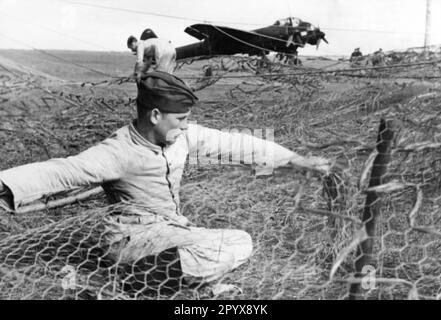 Les membres d'une société de construction construisent des boîtes de camouflage pour les avions de chasse Junkers Ju 88 Luftwaffe. Le treillis métallique est recouvert de matériau de camouflage pour dissimuler les avions de la reconnaissance pendant la journée sur l'aérodrome de champ. L'avion en arrière-plan porte une couche sombre de peinture pour les opérations de nuit contre les îles britanniques. Photo Göricke. [traduction automatique] Banque D'Images