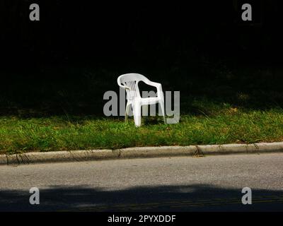 Une chaise blanche vide est assise près du bord de la route. Banque D'Images