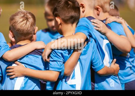 Les enfants motivés dans l'équipe de football applaudissent sur le terrain. Les joueurs qui se jouent dans un cercle sur le terrain. Coach parlant à un groupe de joueurs de football. Joyeux football Banque D'Images