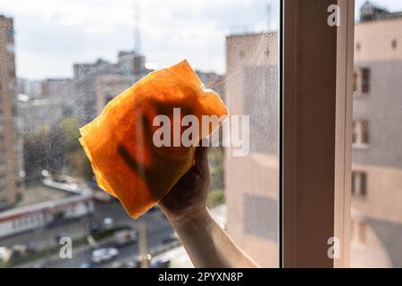 essuie-mains de sexe masculin sur le côté extérieur sale du verre de fenêtre avec un chiffon dans une maison urbaine en hauteur l'après-midi ensoleillé du printemps Banque D'Images