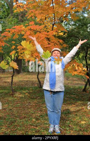 Dans la photo, une jolie fille jette des feuilles d'érable jaune dans l'air dans un parc d'automne. Banque D'Images