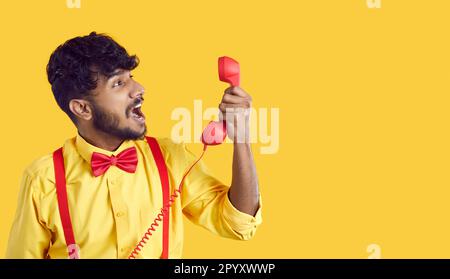 Un jeune homme sud-asiatique criait bruyamment en tenant un téléphone fixe nerveux lors d'un appel d'assistance Banque D'Images