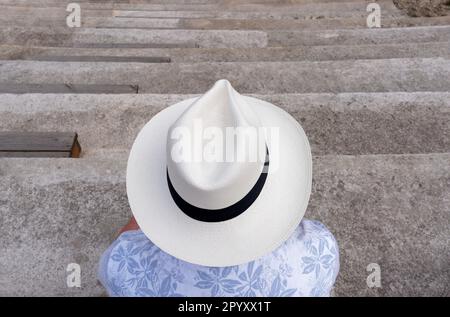 Un homme portant une chemise bleue et un grand chapeau de Panama beige sur sa tête, assis sur quelques marches de pierre et avec son dos à la caméra. Cadix, Espagne Banque D'Images