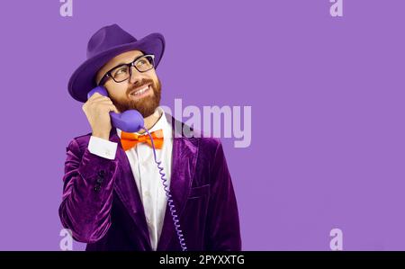 Drôle jeune homme parlant au téléphone et souriant sur fond violet de l'espace de copie Banque D'Images