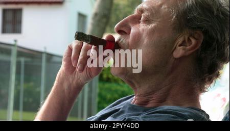 Un homme plus âgé qui profite de sa retraite et qui fume un cigare à l'extérieur Banque D'Images