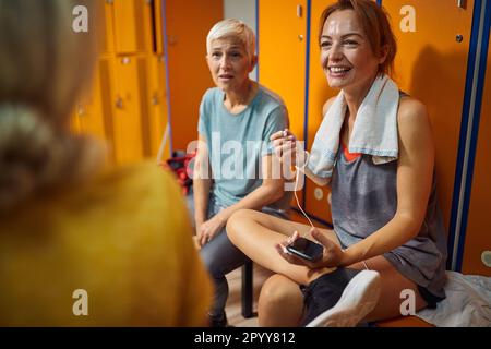 Belle jeune femme avec deux femmes âgées dans le vestiaire de salle de gym ayant une conversation avant la séance d'entraînement, appréciant le temps ensemble. Banque D'Images