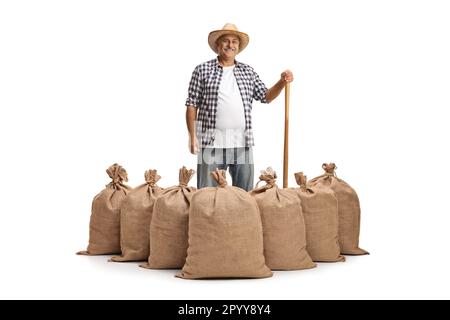 Fermier souriant avec un outil en bois debout derrière des sacs de toile de jute isolés sur fond blanc Banque D'Images