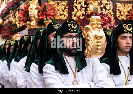 Nazarenos portant des chapeaux verts porte une plate-forme massive avec une statue de Jésus-Christ et les Romains dans une procession pendant la semaine Sainte ou Santa Semana, 5 avril 2023 à Ronda, Espagne. Ronda, établie pour la première fois au 6th siècle avant Jésus-Christ, organise des processions de la semaine Sainte depuis plus de 500 ans. Banque D'Images