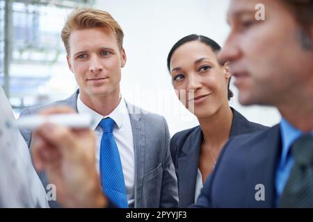 Trouver des idées sur la façon de développer leur activité. Un homme d'affaires écrivant sur un tableau de conférence alors que ses collègues se tiennent à côté. Banque D'Images