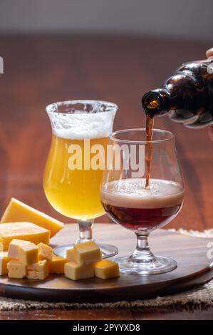 Verres de bière blonde jaune belge et brune foncée fabriqués en abbaye et en bois avec une variété de fromages belges, plats et bières assortis en Belgique Banque D'Images