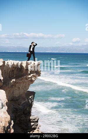 Recherche de nouvelles possibilités à l'horizon. Homme d'affaires debout sur une falaise surplombant l'océan et cherchant l'horizon. Banque D'Images