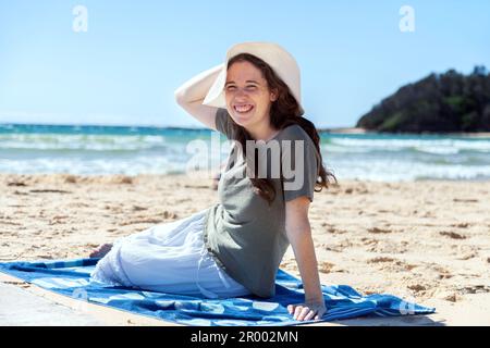 Jeune femme souriante dans sa vingtaine se détendant sur une serviette à la plage australienne le jour ensoleillé Banque D'Images