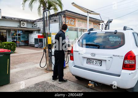 Jeune homme en noir remplissant sa voiture à une station-service rurale dans une ville de campagne australienne Banque D'Images