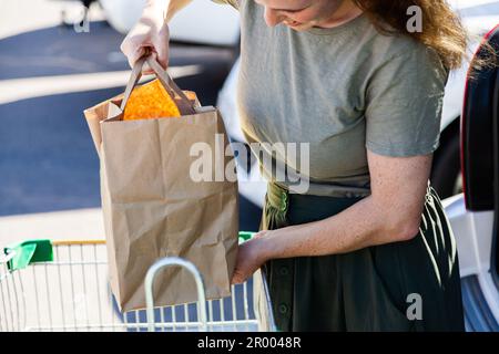 femme chargeant sac de papier d'épicerie dans le coffre de voiture après magasin alimentaire hebdomadaire Banque D'Images