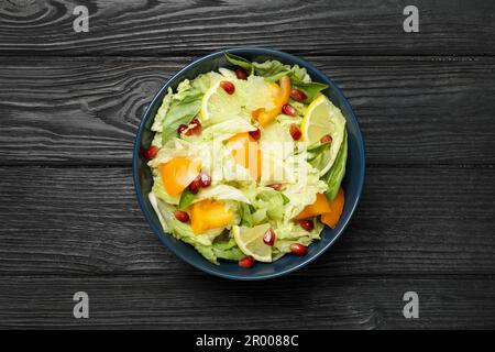 Salade délicieuse aux graines de chou chinois, citron, persimmon et grenade sur une table en bois noir, vue du dessus Banque D'Images