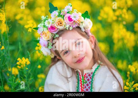 Rêve belle jeune fille avec un chapelet de fleurs, robe folklorique ethnique avec broderie bulgare traditionnelle pendant le coucher du soleil sur un rapseed agricole Banque D'Images