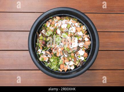 Compostage pile de feuilles et pourriture de la cuisine grattoir avec les déchets de coquilles d'aubergines dans seau noir sur plancher de bois. Banque D'Images