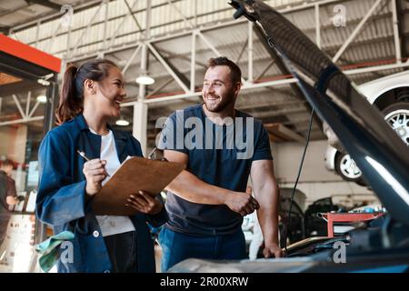 Nous proposons des services pour toutes les marques et tous les modèles. deux mécaniciens travaillent ensemble sur une voiture dans un atelier de réparation automobile. Banque D'Images