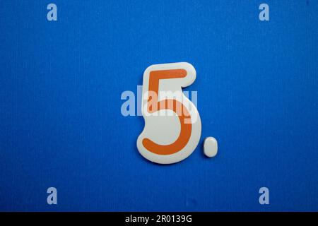 Le numéro 5, placé sur un fond bleu, photographié d'en haut, de couleur orange et blanche. Banque D'Images