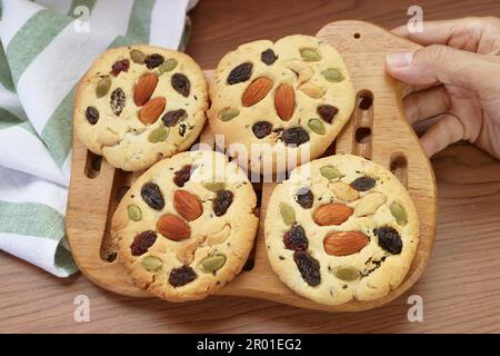 Placez à la main une grille en bois de biscuits d'amande et de raisin fraîchement cuits sur la table Banque D'Images