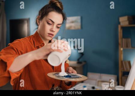 portrait en gros plan d'une jeune artiste brésilienne dans un studio situé près d'une toile de peinture blanche sur une palette. Cheveux noirs, habillés Banque D'Images