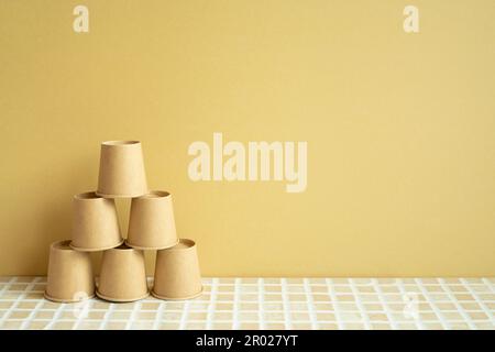 Pile pyramidale de gobelets bruns sur le bureau. arrière-plan jaune. développement de l'entreprise concept de croissance de la réalisation Banque D'Images