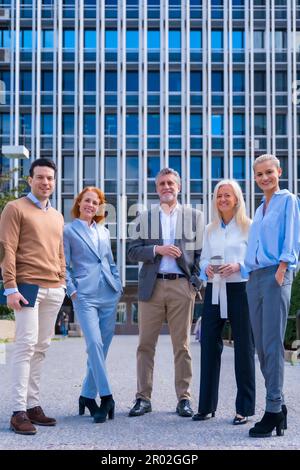 Portrait d'un groupe joyeux de collègues marchant à l'extérieur dans un bureau d'entreprise, avec un bâtiment de bureau en arrière-plan Banque D'Images