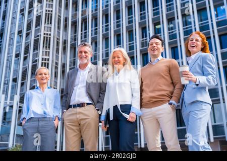 Portrait d'un groupe joyeux de collègues marchant à l'extérieur dans un bureau d'entreprise en riant Banque D'Images