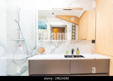 Maison salle de bains, lumineux intérieur de salle de bains avec douche en verre carrelée, meuble-lavabo, intérieur conçu avec bois brun foncé Banque D'Images