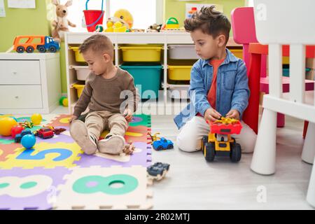 Adorables garçons jouant avec des voitures jouet et tracteur assis sur le sol à la maternelle Banque D'Images