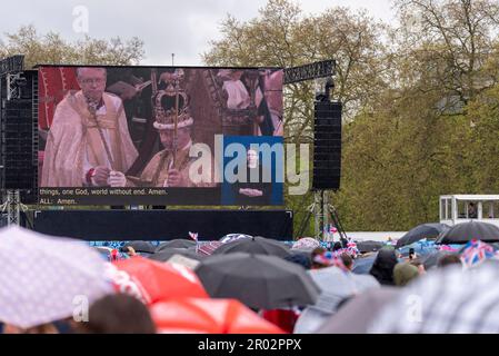 Hyde Park, Westminster, Londres, Royaume-Uni. 6th mai 2023. Un grand nombre de personnes sont venues à Londres pour le couronnement. De grands écrans ont été installés à Hyde Park pour les nombreux qui ne pouvaient pas s'adapter aux zones autour de la route de procession. Une grande partie de l'événement a eu lieu par temps humide. Des gens sous des parasols au moment du couronnement du Roi Banque D'Images