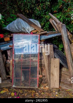 Une vieille fenêtre rouge écartée encadrée placée parmi différents objets, reflète le ciel de l'après-midi dans une ferme près de la ville d'Arcabuco dans le centre de la Colombie. Banque D'Images
